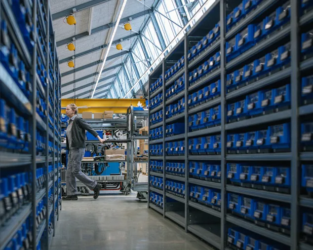 Ein Mann schreitet durch ein Lager, in dem sich zahlreiche blaue Behälter befinden.
