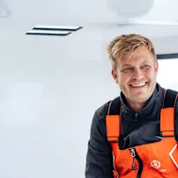 Smiling Oliver Heer in an orange and black life vest aboard a white boat with windows visible in background.