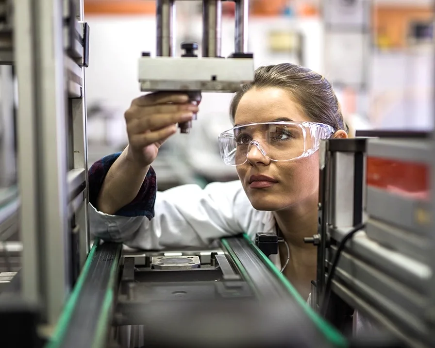 En kvinde i en laboratoriekittel arbejder koncentreret ved en maskine i et moderne laboratorium.