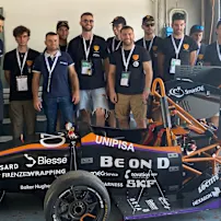 A group of people in matching shirts stand around a black and orange race car with the number 120 and various sponsor logos.