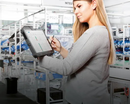 Une femme tient une tablette avec des instructions d'assemblage numériques dans un environnement de fabrication moderne.