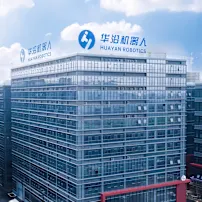 Modernes Glasbürogebäude mit Huayan Robotics Logo und chinesischem Text auf dem Dach vor blauem Himmel mit weissen Wolken.