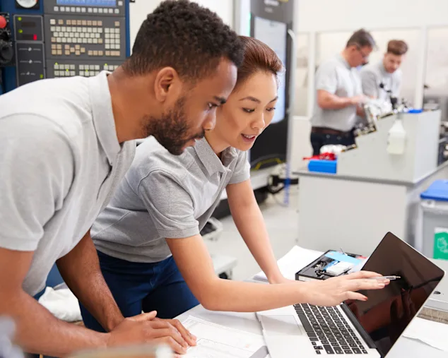 Zwei Ingenieure unterhalten sich und überprüfen gemeinsam Testergebnisse auf einem Laptop in einem technischen Labor.