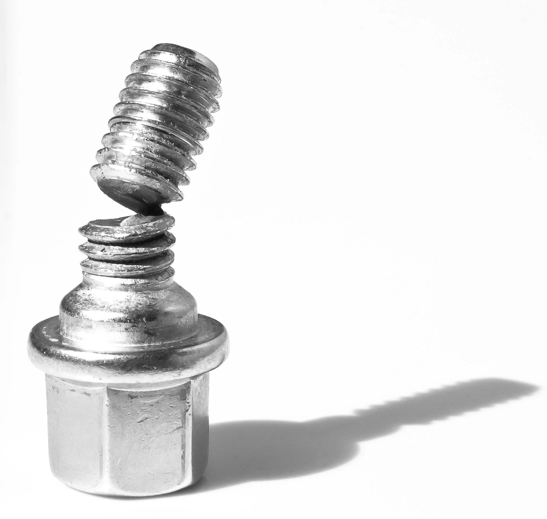 一顆斷裂的螺栓顯示出螺紋的材料疲勞,並在白色表面上投下陰影。