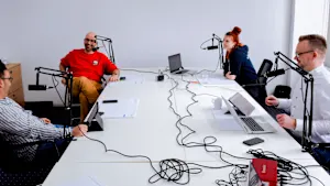 Négy személy ül egy asztalnál, mindegyikük előtt mikrofon, egy beszélgetés vagy interjú keretében.