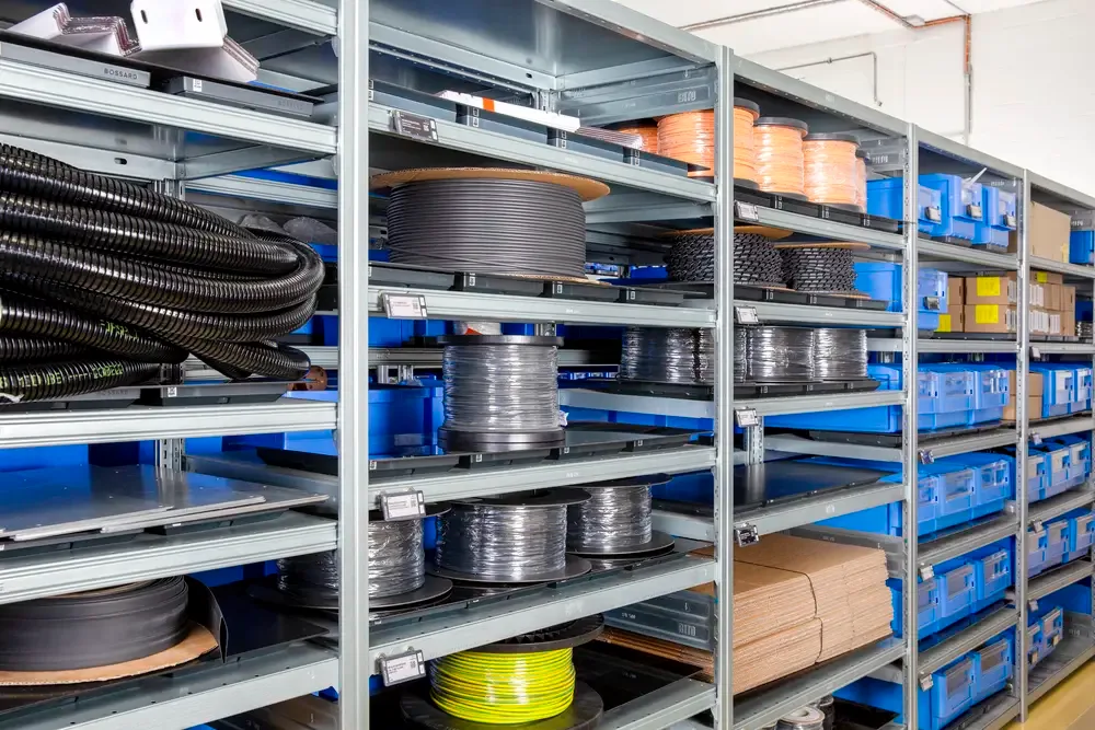 금속 랙에 대형 케이블 릴, 튜빙 및 파란색 보관함이 정리된 산업용 창고 선반.