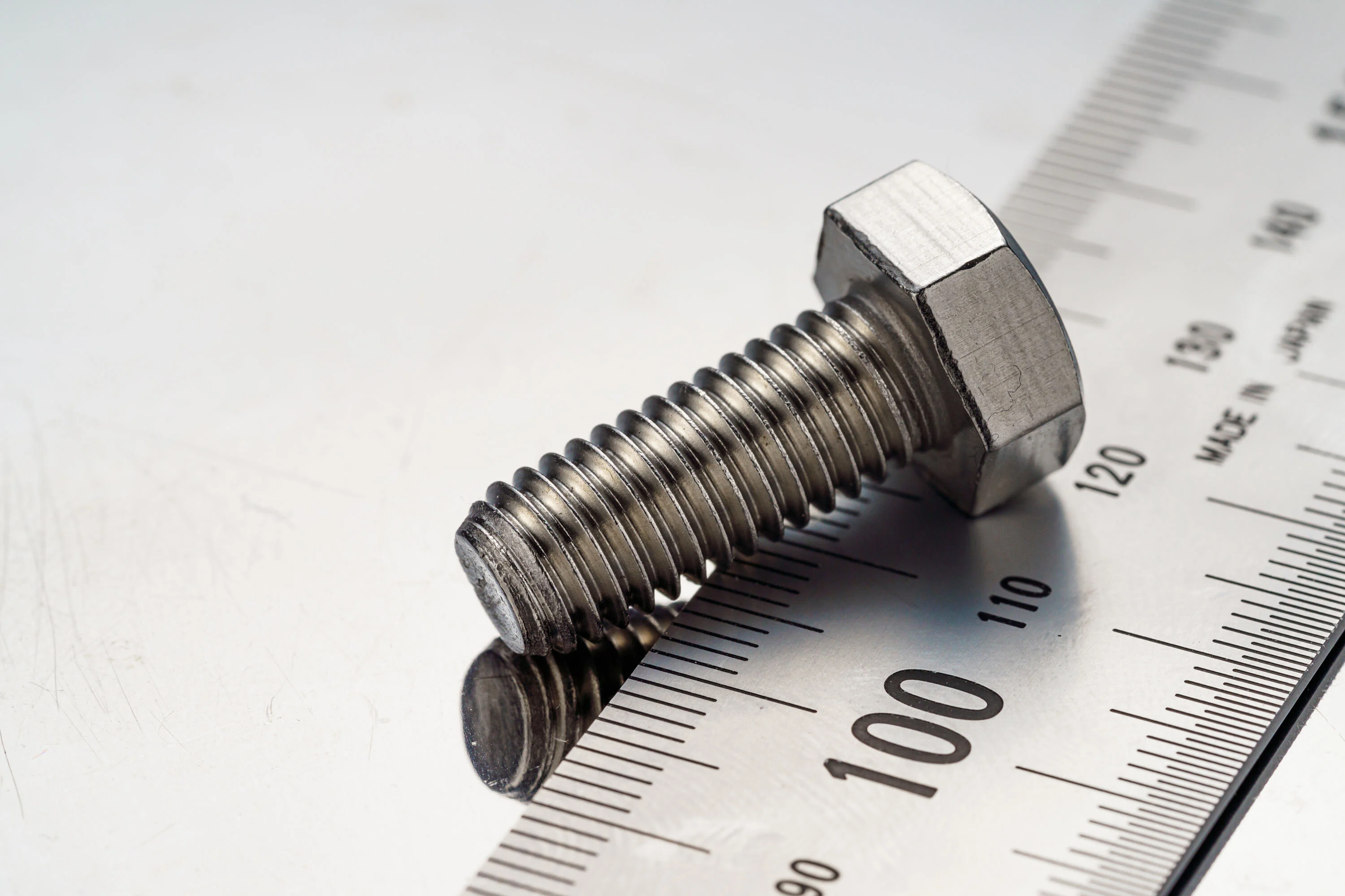 Tornillo de acero en primer plano sobre placa de metal con regla