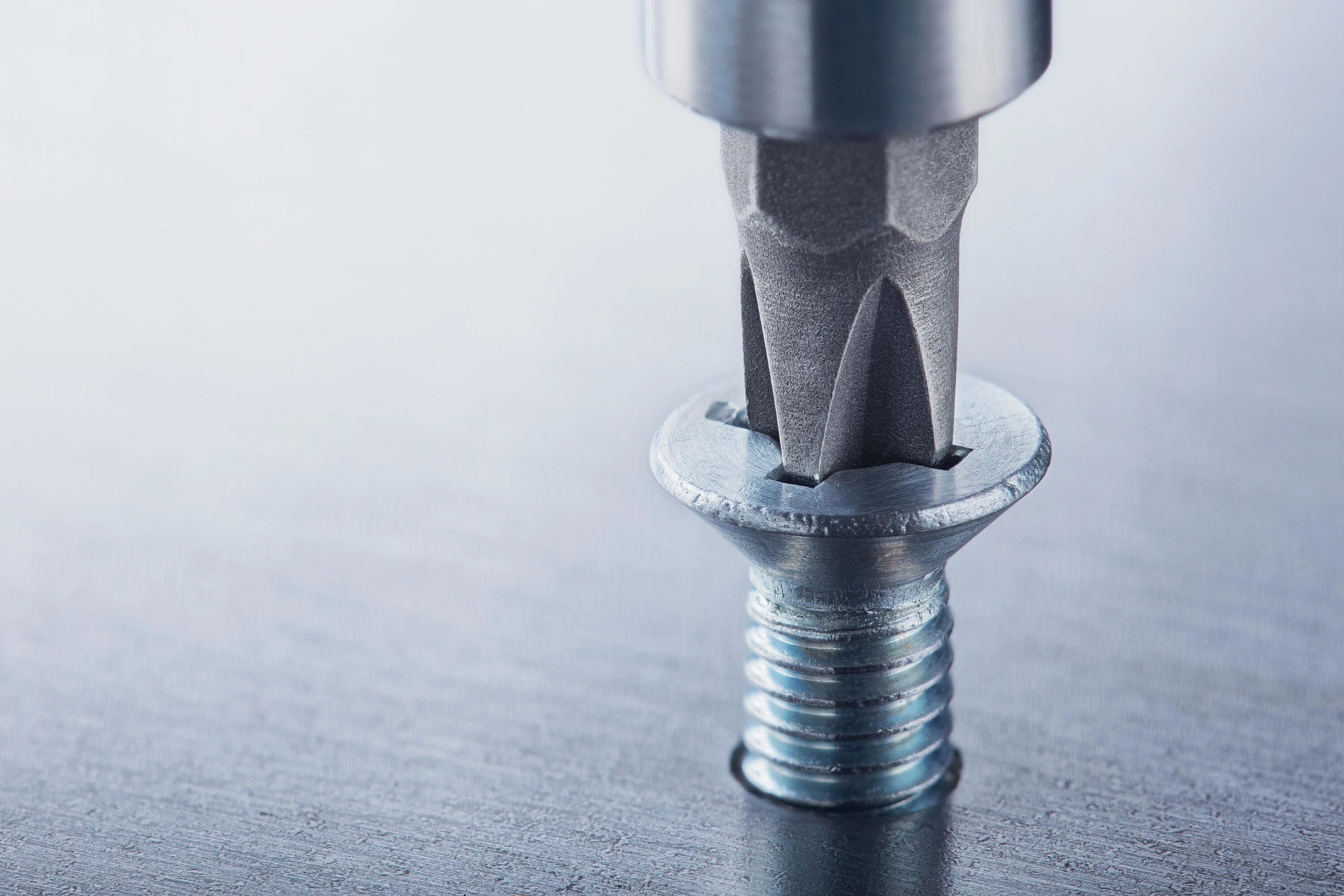 A screw with a cross recess drive is screwed into a metal plate.