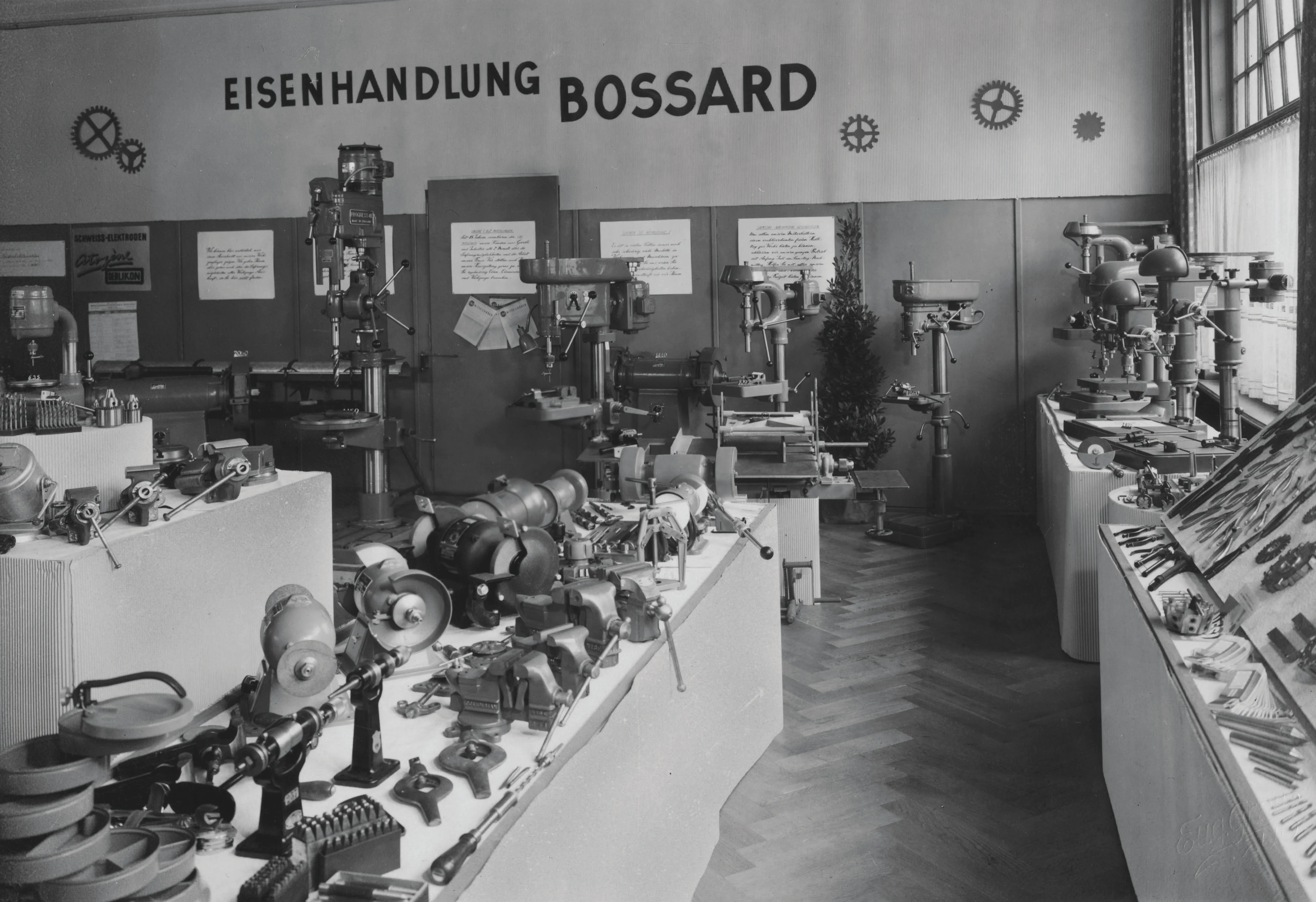 Et vintage sort-hvidt foto af en Bossard jernvarebutik fra 1930'erne fyldt med forskellige værktøjer og udstyr.