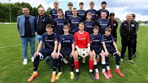 Jugendfußballmannschaft der TSG Achstetten mit Trainern in neuen dunkelblauen Bossard-Trikots auf dem Fußballplatz.