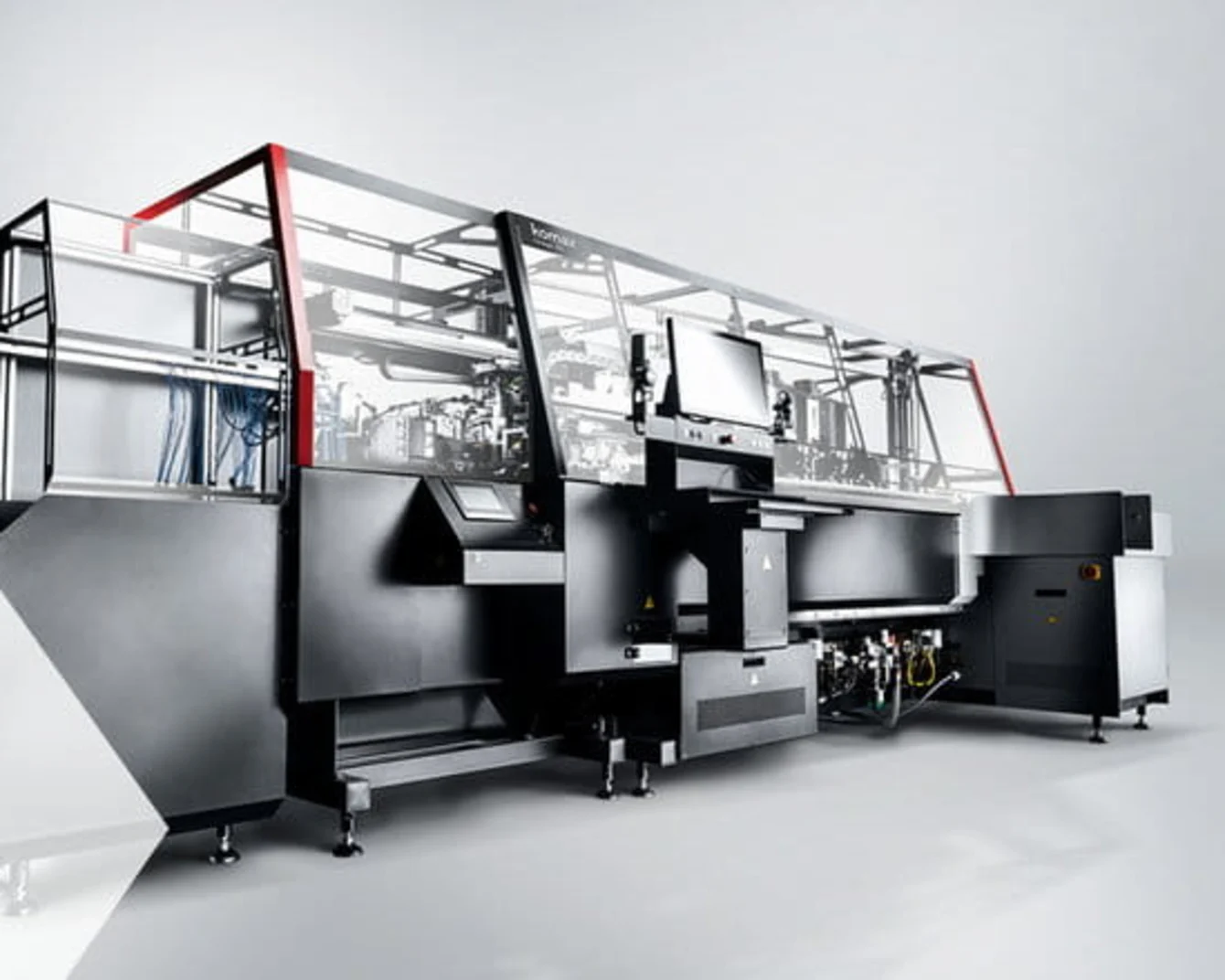 Large industrial machine with a sleek black and silver design, featuring a computer screen and red accents, on a gray background.