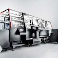 Große Industriemaschine mit elegantem schwarz-silbernem Design, ausgestattet mit einem Bildschirm und roten Akzenten, auf grauem Hintergrund.