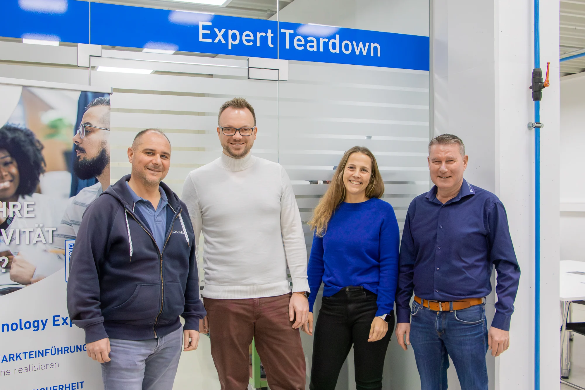 Marcus Ritter, Tobias Engelberg, Maja Matzke und Horst Sälzle stehen nebeneinander vor einer matt folierten Sichtschutzscheibe mit der Aufschrift "Expert Teardown"