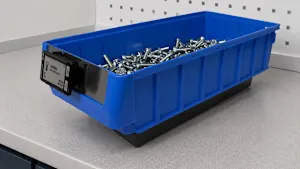 Bac de rangement en plastique bleu rempli d'éléments d'assemblage, sur surface de travail grise.