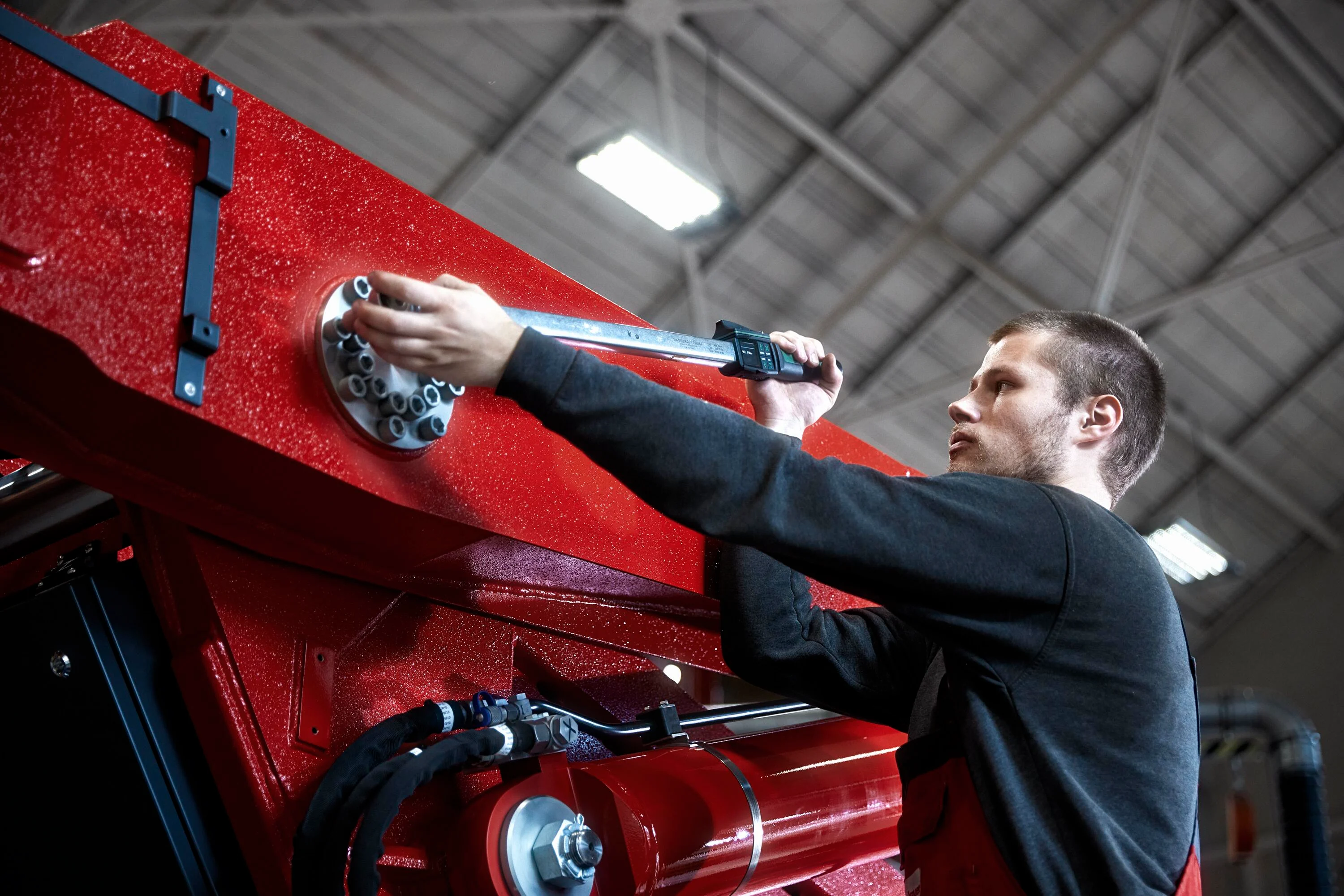 Maintenance worker in a black shirt tightens the screw of a heavy machine with a digital torque wrench.