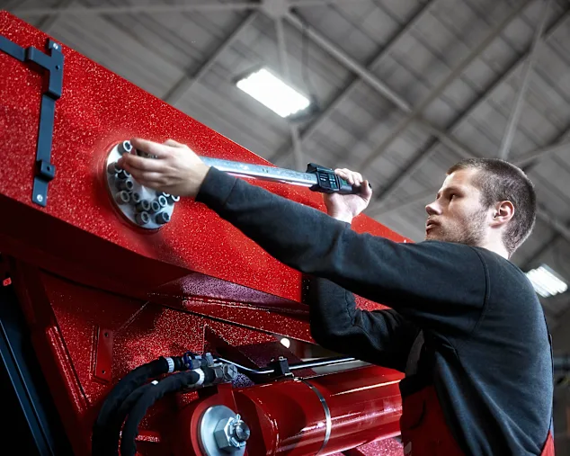 Maintenance worker in a black shirt tightens the screw of a heavy machine with a digital torque wrench.