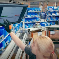 Young assembly worker checking work instructions on a computer screen with Bossard SmartBins in the background.