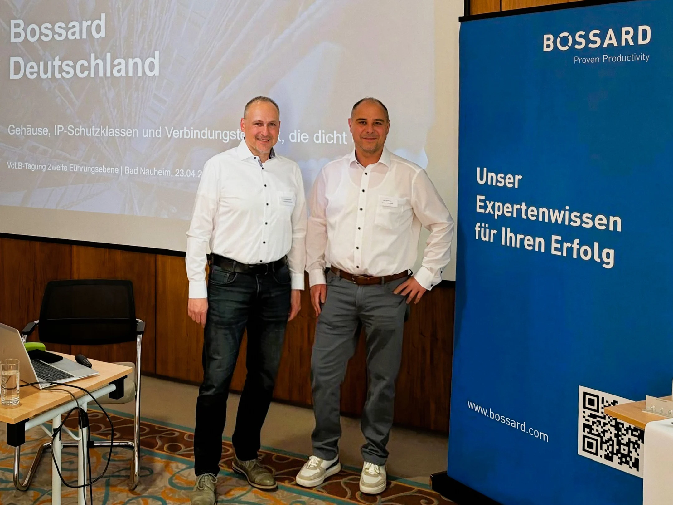 Matthias Kreuter steht neben Marcus Ritter vor einer Beamerwand mit der Aufschrift Bossard Deutschland. Rechts daneben ein blaues Banner mit der Aufschrift "Unser Expertenwissen für Ihren Erfolg"