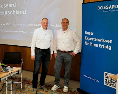 Matthias Kreuter steht neben Marcus Ritter vor einer Beamerwand mit der Aufschrift Bossard Deutschland. Rechts daneben ein blaues Banner mit der Aufschrift "Unser Expertenwissen für Ihren Erfolg"