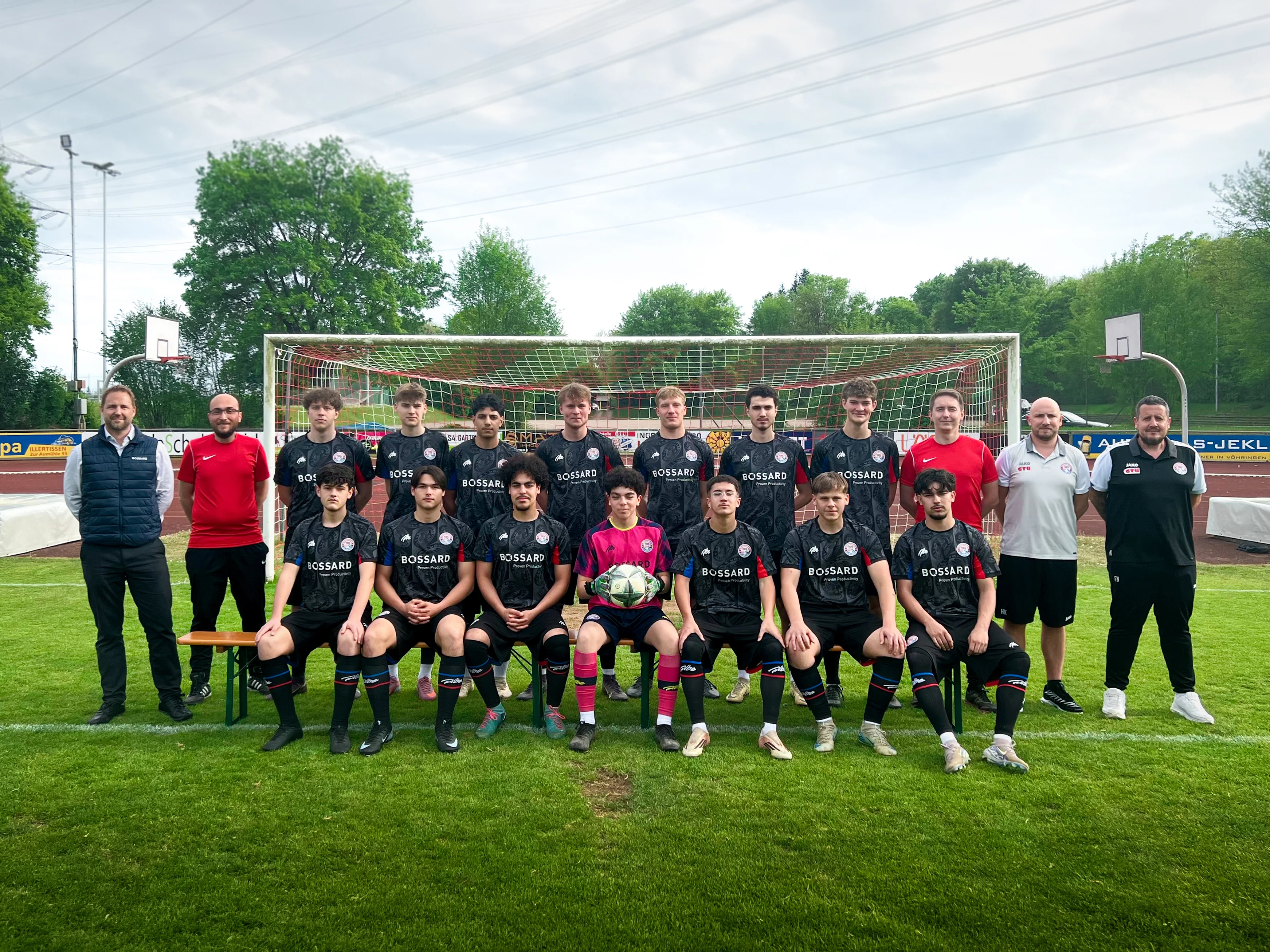 Mannschaftsfoto des SC Vöhringen auf dem Fußballplatz vor einem Tor, mit Spielern und Betreuern in Bossard-Trikots.
