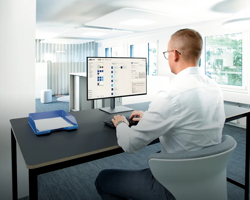 Un homme assis à un bureau, concentré sur son écran d'ordinateur, absorbé par son travail.