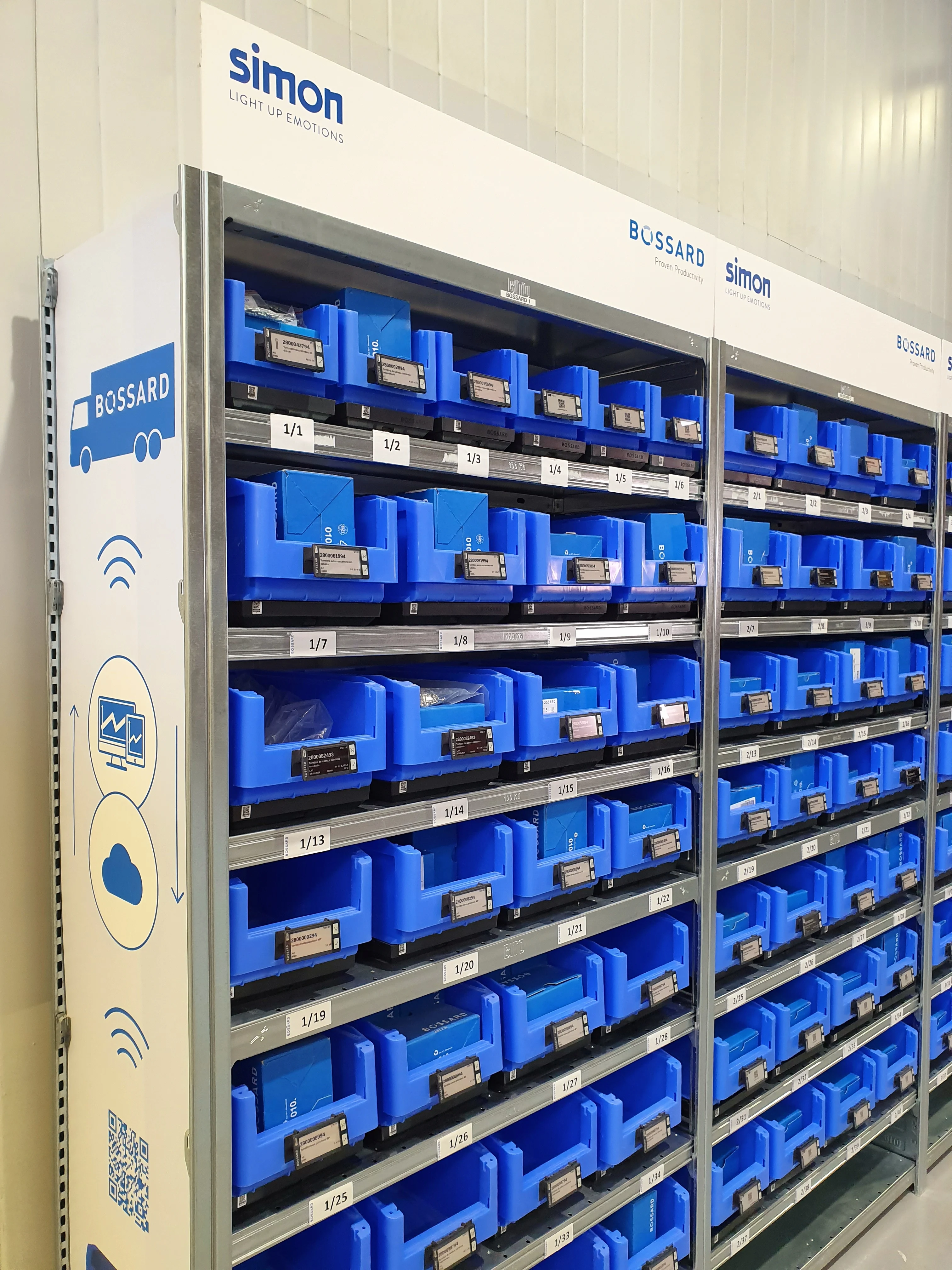 Estantes llenos de contenedores azules organizados, cada uno etiquetado con números, en un área de almacenamiento con la marca "Simon" y "Bossard".