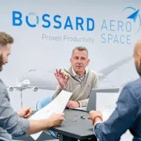 3 personnes examinant la conception et les éléments d'assemblage avec un arrière-plan mural Bossard Aerospace
