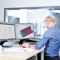 Ein Mann in einem blauen Hemd arbeitet an einer technischen Zeichnung an einem Stehpult am Computer.