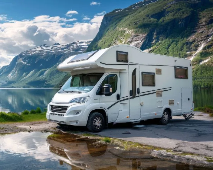 Ein weißes Wohnmobil steht am Ufer eines Sees, sommerliche Berglandschaft im Hintergrund.