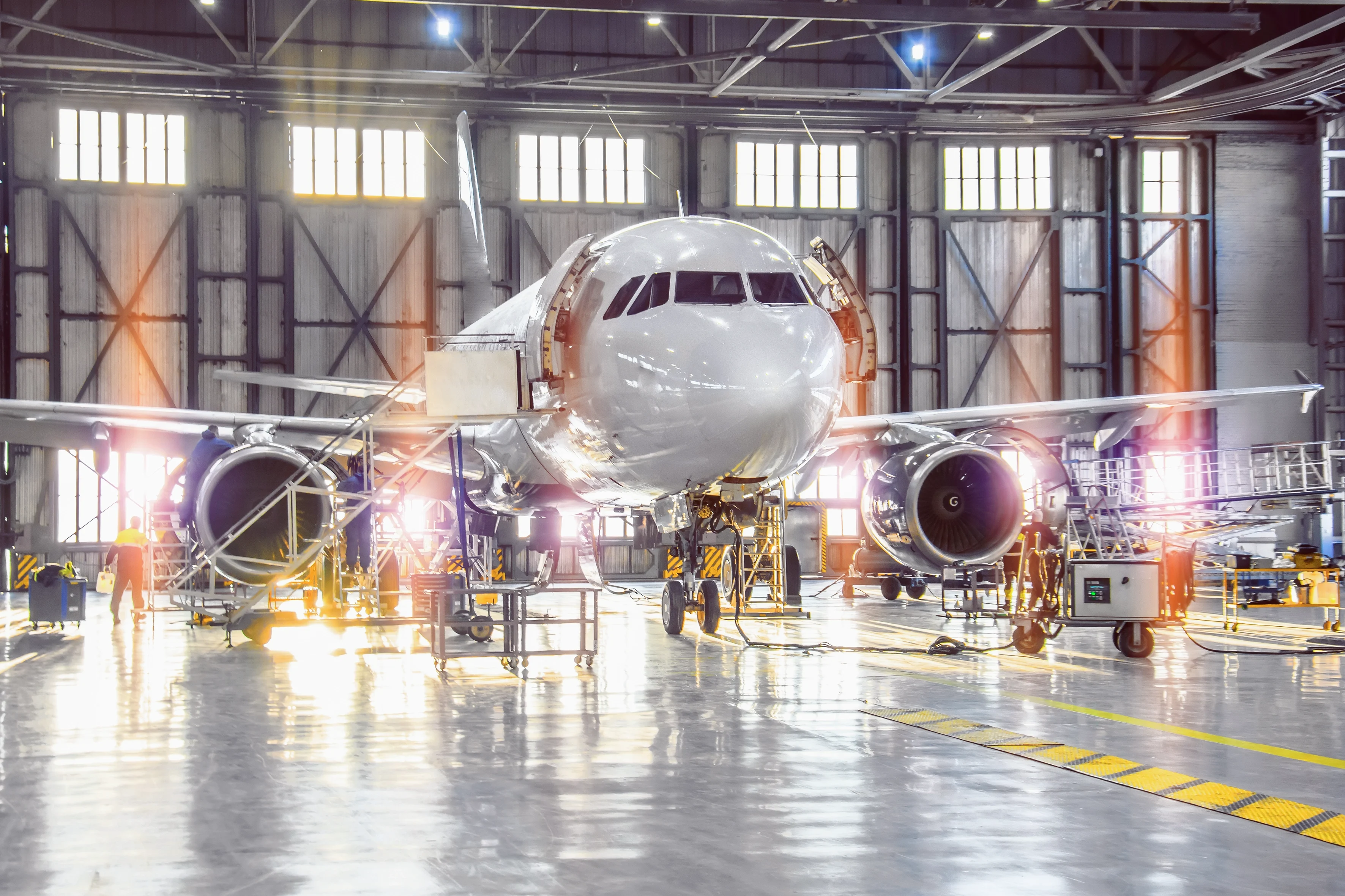 Un avion en maintenance dans un hangar spacieux, avec des techniciens et des outils visibles autour.