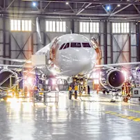 An airplane undergoing maintenance inside a spacious hangar, with technicians and tools visible around it.