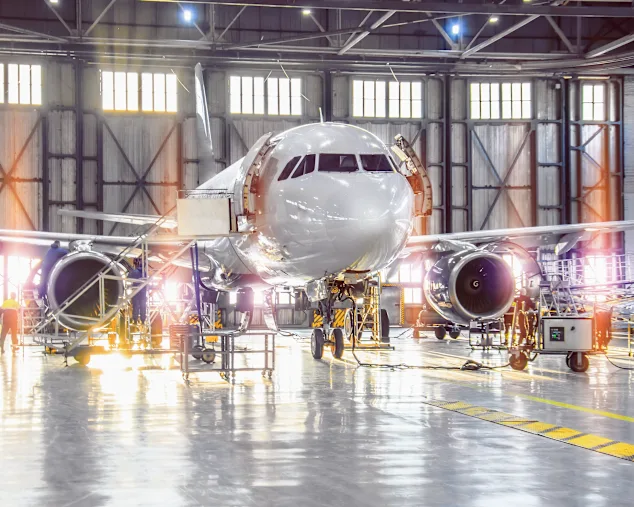 Un avion en maintenance dans un hangar spacieux, avec des techniciens et des outils visibles autour.