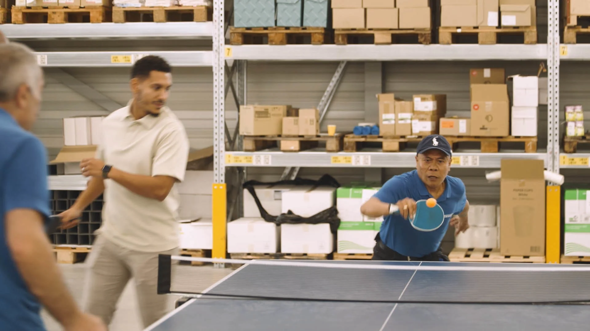 A men is engaged in a competitive game of ping pong inside a spacious warehouse setting.