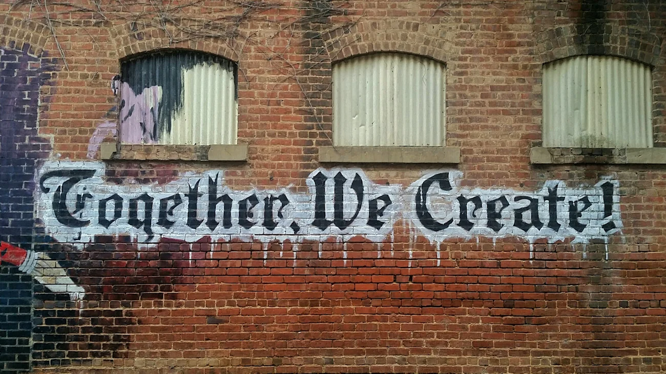 กำแพงอิฐที่มีพื้นผิวพร้อมกราฟฟิตีสีขาวดำที่เขียนว่า "together we create!" ในสไตล์ศิลปะ