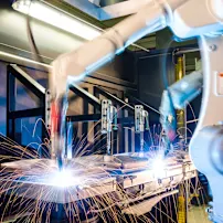 Industrial robotic arms welding metal with bright orange sparks flying in a modern automated manufacturing facility.