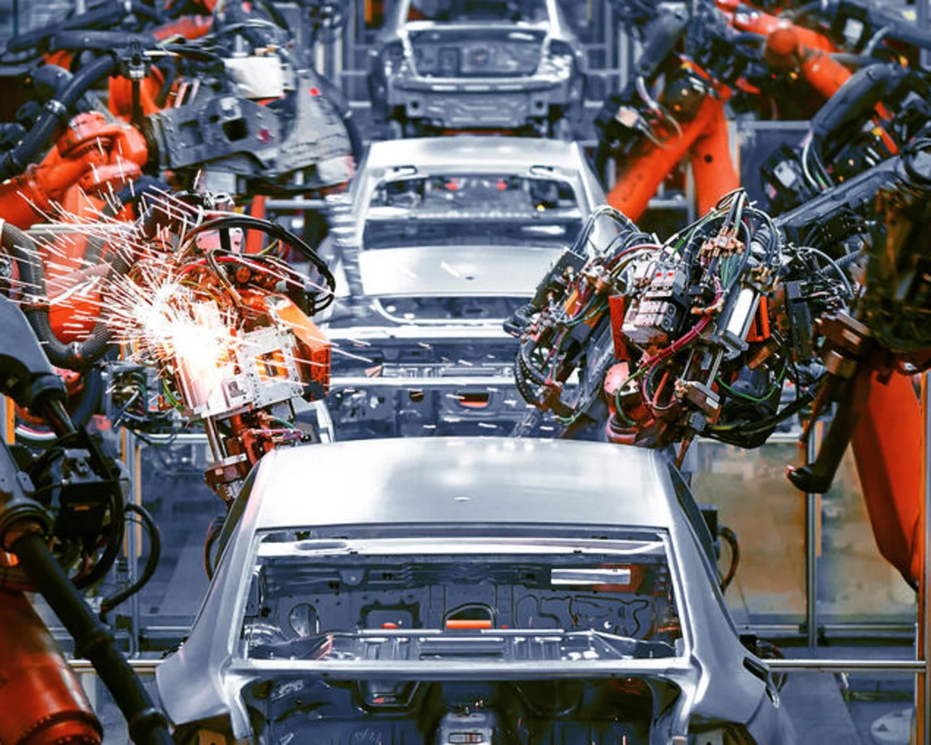 橙色和黑色機械手臂在汽車裝配線上焊接白色車身,焊接點火花四濺。