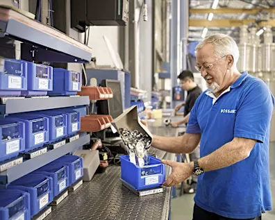 Bossard employee in blue shirt refilling SmartBin container at stock location.