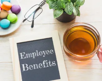 Employee benefits written on a small blackboard lying on the table next to a cup of tea