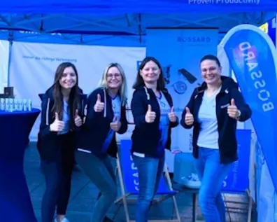 Vier lächelnde Frauen vor einem blauen Bossard-Zelt bei einer Veranstaltung