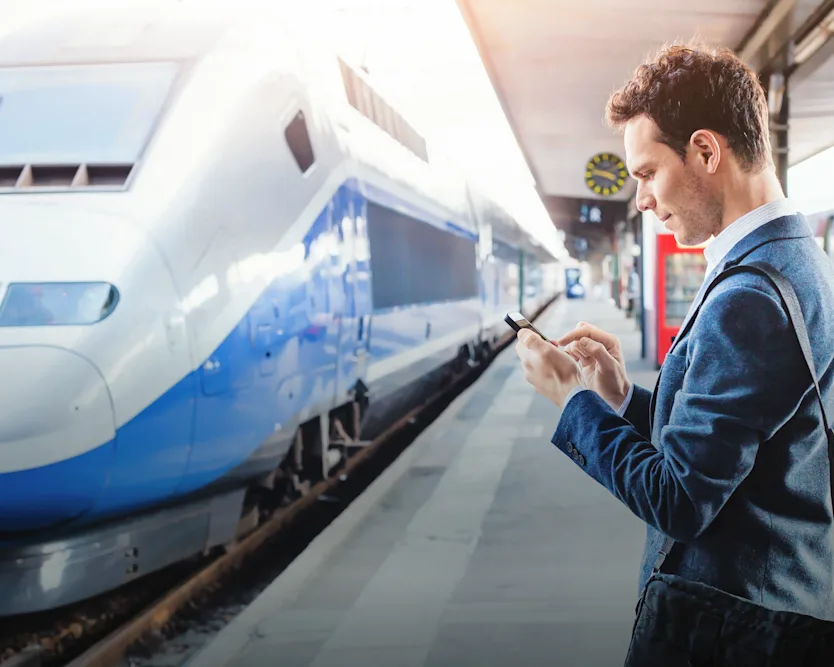 Ein Mann auf einem Bahnhof, der ein elektronisches Gerät benutzt.