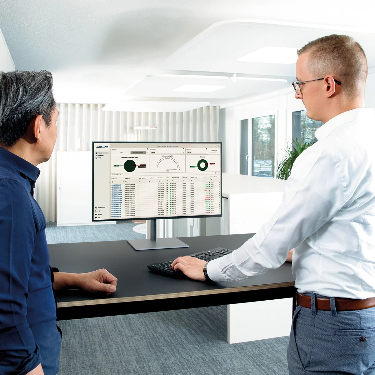 To mænd ved et skrivebord, fokuseret på en computerskærm, der viser en datarapport.