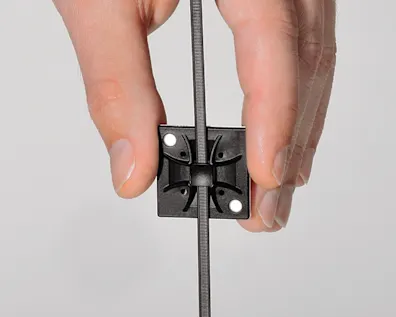 Tay cầm một giá đỡ cáp HellermannTyton Q-Mount màu đen để cố định dây cáp vào vị trí.