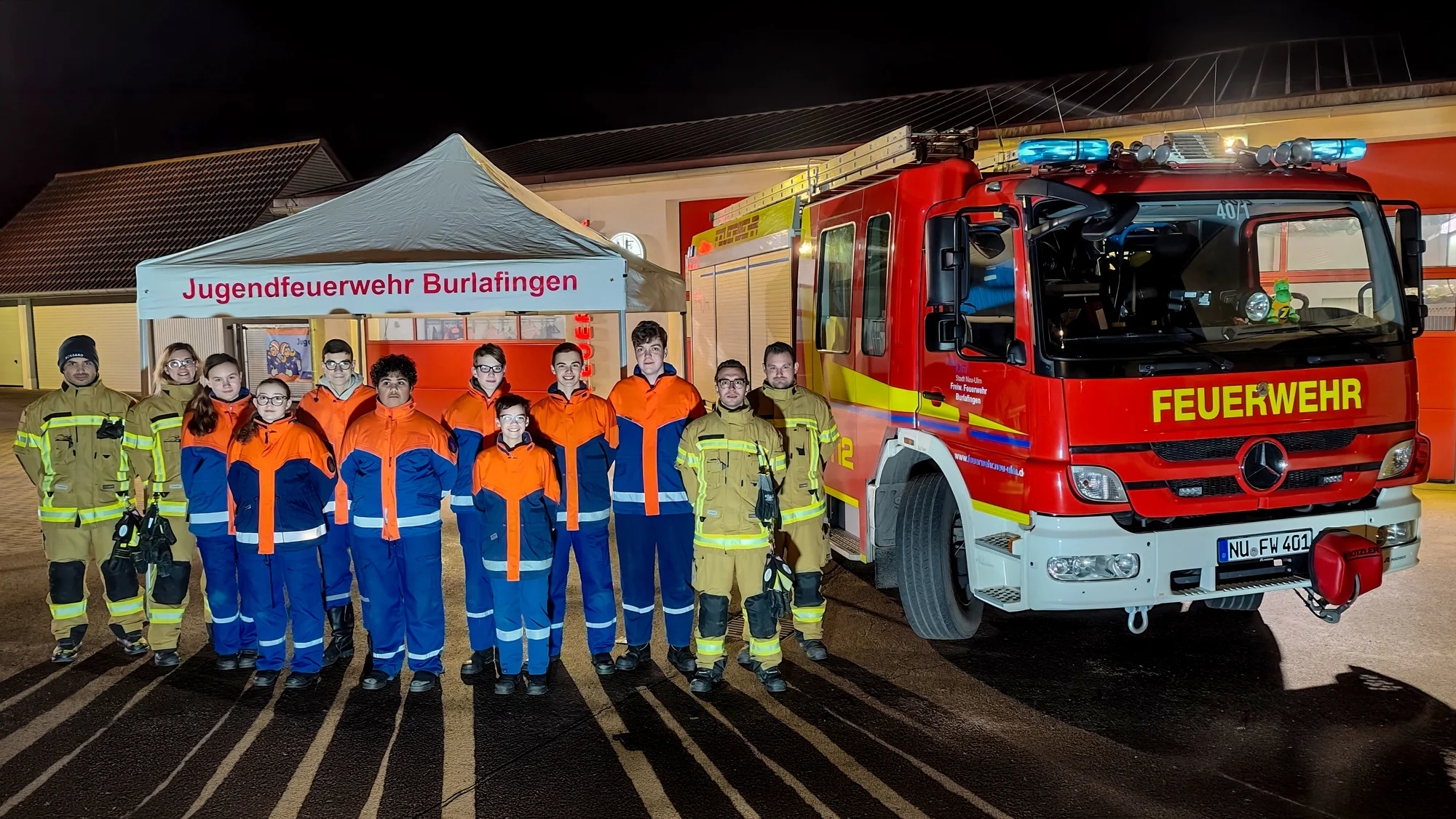 Gruppenfoto der Jugendfeuerwehr Burlafingen mit Feuerwehrfahrzeug und Zelt bei einer Veranstaltung am Abend.