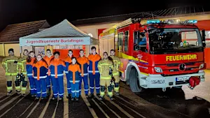 Gruppenfoto der Jugendfeuerwehr Burlafingen mit Feuerwehrfahrzeug und Zelt bei einer Veranstaltung am Abend.