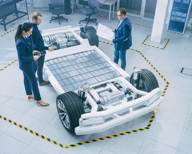 A woman and two men standing in front of an electric car chassis with solar panels.