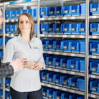 Ein Mann und eine Frau stehen vor einem Regal mit blauen Bossard SmartBins bei Weibel.