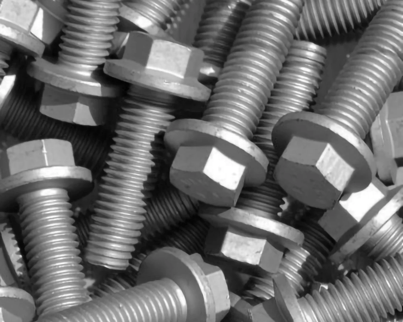 Close-up photograph of multiple metal bolts with hexagonal heads and threaded shafts scattered in a pile.