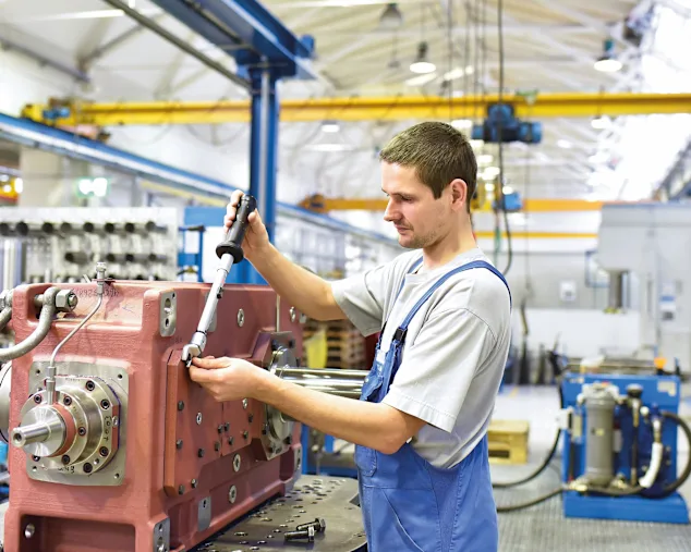Young assembly worker in a gear manufacturing factory holding a torque wrench.