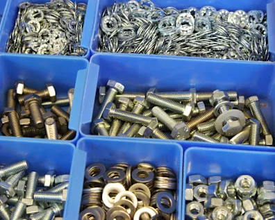 Blaue Sichtlagerkästen mit sortierten Metallteilen wie Schrauben, Muttern, Unterlegscheiben und Sicherungsringen.