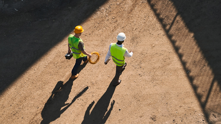 Two people with hard hats walking on dirt